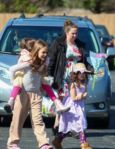 A mother and her two daughters crossing the church lot, flowers in hand