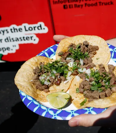 A plate of street tacos handed across, in front of a shirt printed with Jeremiah 29:11
