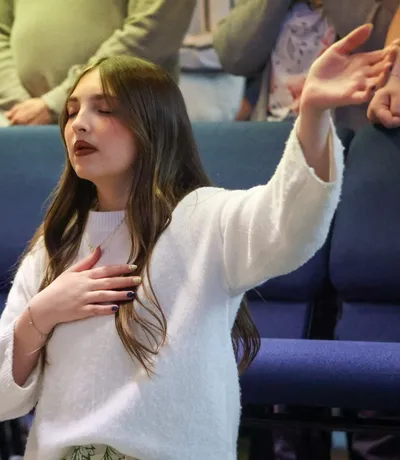 A young woman with one hand on her heart and the other raised