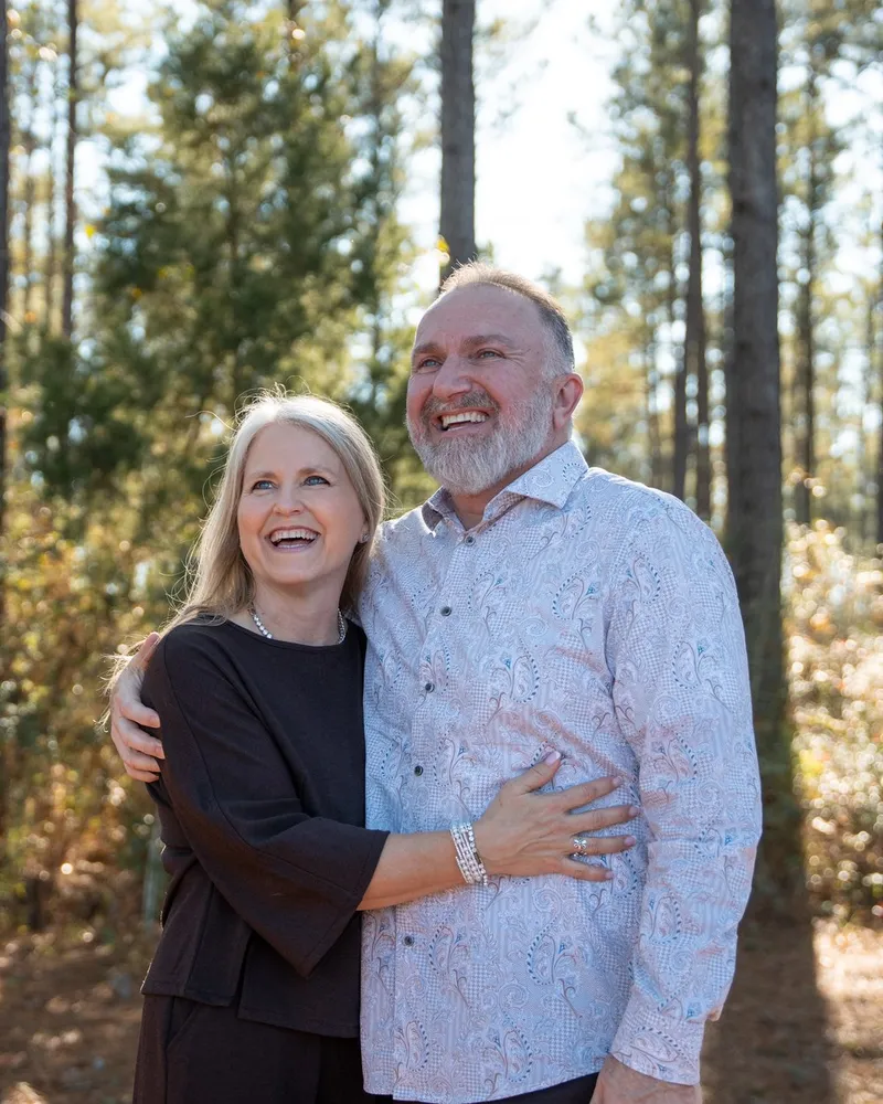 Pastors James and Cathie Hightshoe laughing together outdoors among the pines